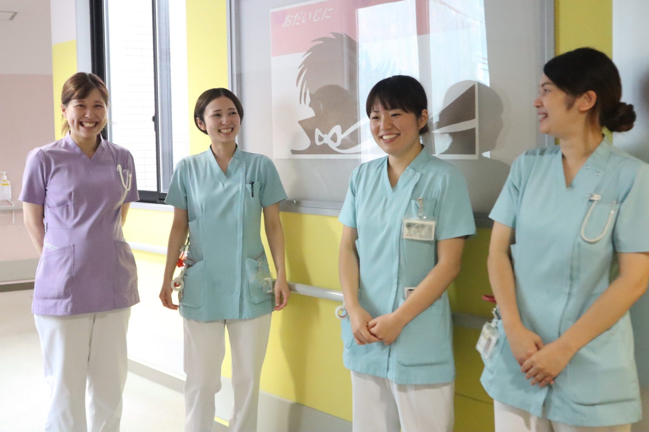 介護施設のスタッフ4名が廊下で笑顔で立っている風景